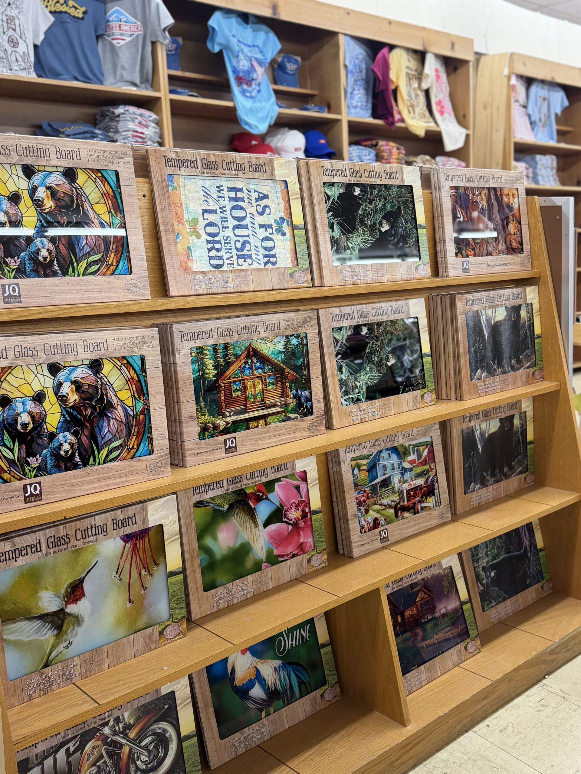 Display of tempered glass cutting boards featuring black bears, hummingbirds, cabins, farm scenes, and Smoky Mountain wildlife artwork inside a Tennessee gift shop.